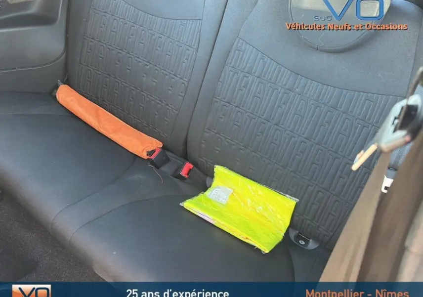 Vue intérieure sur la banquette arrière noire embossée du logo FIAT avec un gilet jaune et un triangle de signalisation.