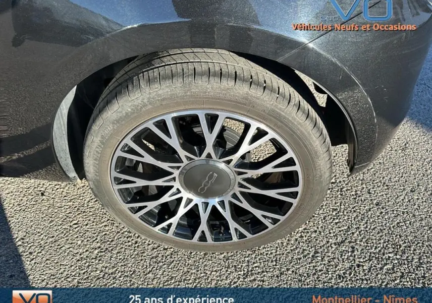 Gros plan sur la roue avant gauche d'une FIAT 500C noire 2024, mettant en valeur la jante au design complexe.