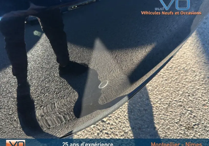 Reflet d'une personne debout sur le capot noir brillant d'une Fiat 500C 2024 hybride, vue rapprochée extérieure.