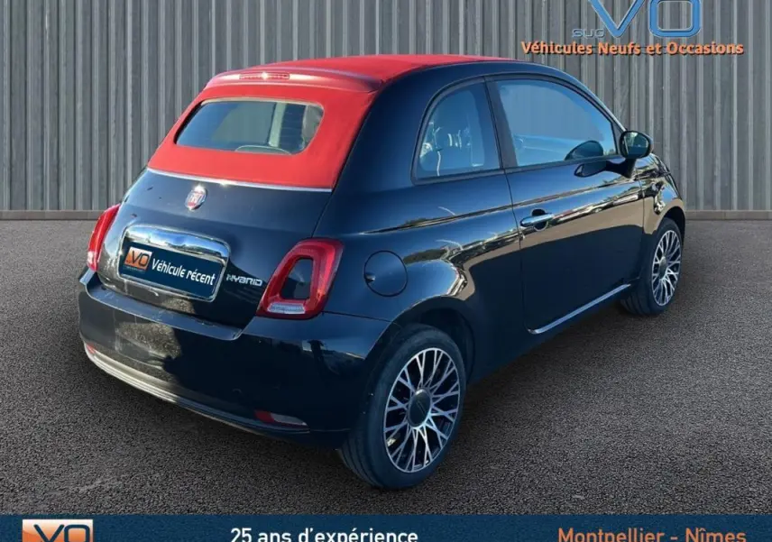 Vue 3/4 arrière droite d'une FIAT 500C noire 2024 avec toit rouge et jantes stylisées, version hybride essence.