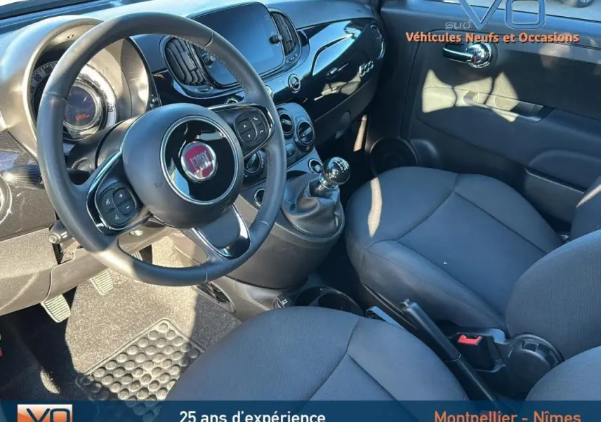 Intérieur du Fiat 500C 2024 noir, vue côté conducteur montrant le volant, tableau de bord et levier de vitesse manuel.
