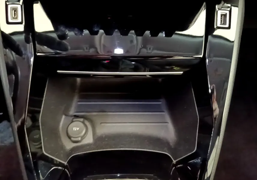 Gros plan sur la console centrale noire du Peugeot 2008 avec prise 12V et finition brillante autour.
