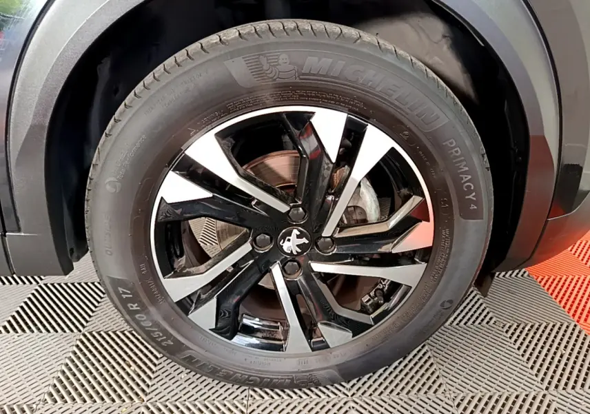 Gros plan sur la roue avant gauche du Peugeot 2008 noir, mettant en valeur la jante alliage bicolore et le pneu Michelin.