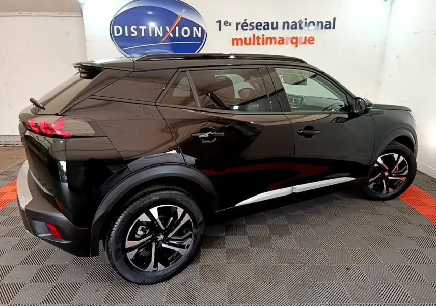 Vue 3/4 arrière droite d'un Peugeot 2008 noir 2021 avec jantes noires et toit noir brillant dans un showroom.