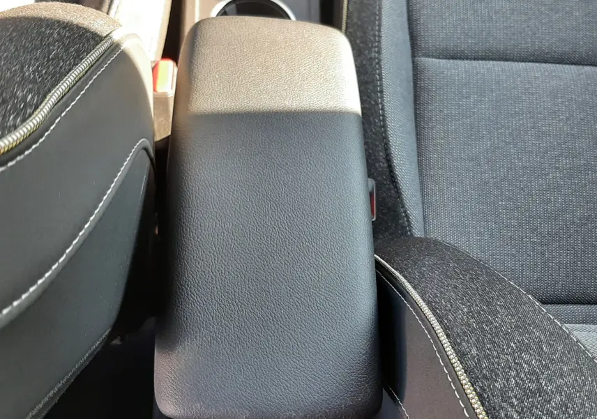 Vue plongeante sur l'accoudoir central noir et les sièges tissu gris du Renault Captur II 2025 finition Techno.