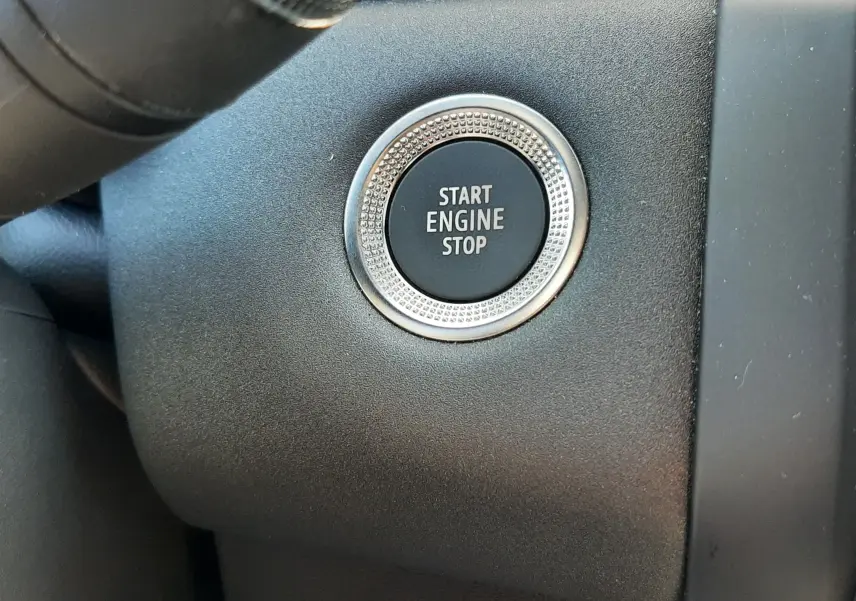 Gros plan sur le bouton Start Engine Stop entouré d’un anneau métallique, tableau de bord noir du Renault Captur gris Cassiopée.