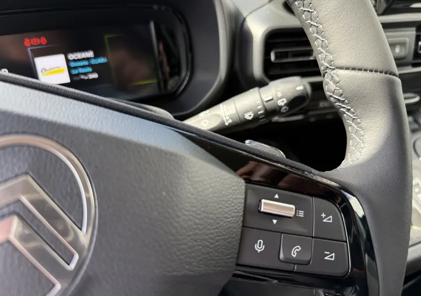 Gros plan sur le volant cuir gris du Citroën Berlingo 2026 avec commandes multifonctions et tableau de bord numérique partiel.
