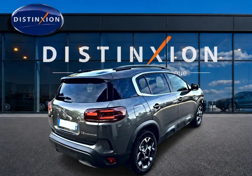 Vue 3/4 arrière droite d'un Citroën C5 Aircross gris 2025 avec jantes alu et vitres arrière teintées, devant un showroom.
