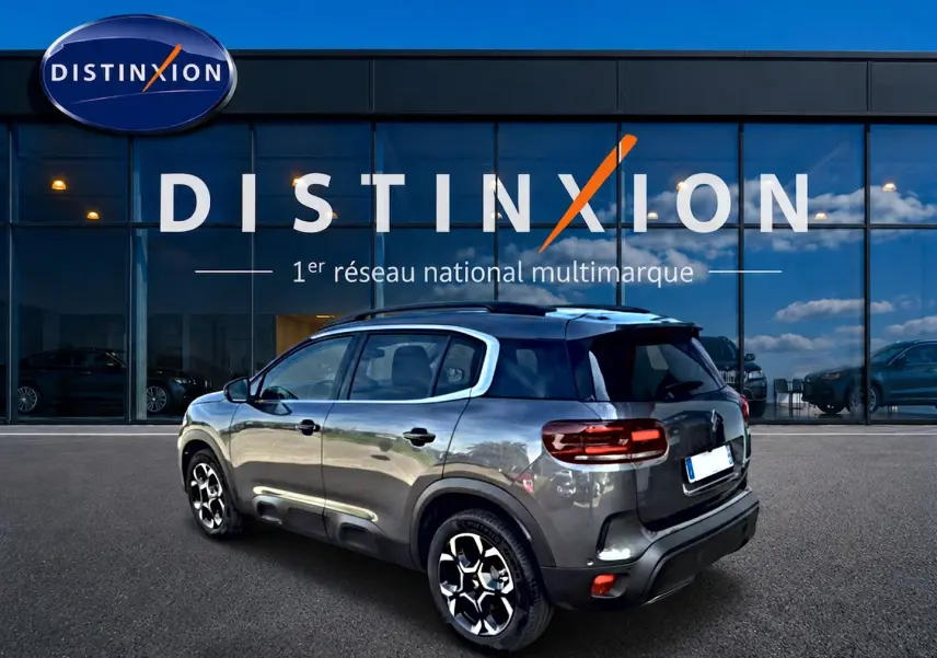 Citroën C5 Aircross gris vue 3/4 arrière droit, avec jantes alliage et barres de toit visibles devant un showroom Distinxion.