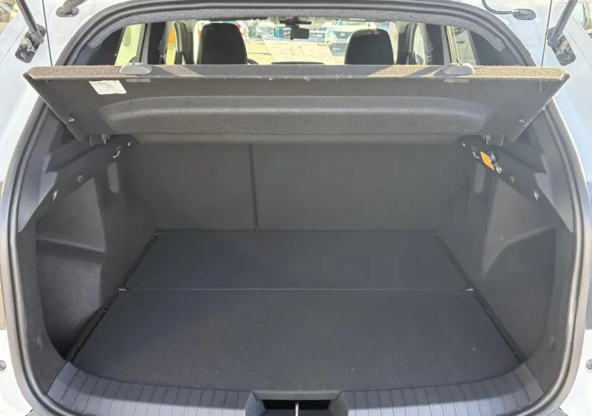 Coffre ouvert du Dacia Duster blanc métallisé 2024, vue arrière montrant l'espace de chargement vide et la tablette cache-bagages relevée.