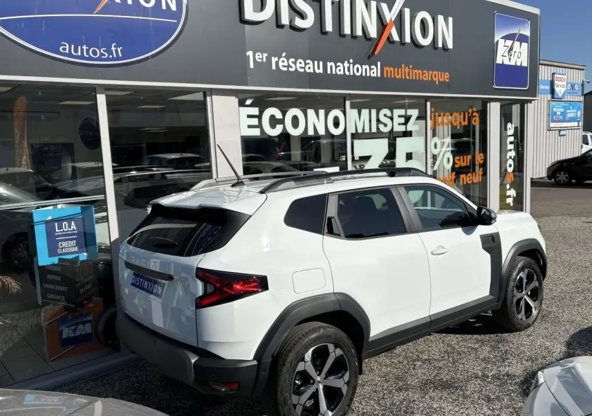 Vue 3/4 arrière droite d'un Dacia Duster blanc métallisé avec barres de toit noires et jantes alliage 18 pouces.