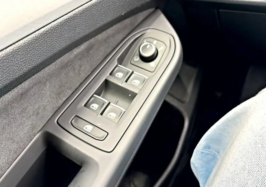 Gros plan sur la commande des vitres électriques côté conducteur d'une Volkswagen Golf noire, intérieur tissu gris.