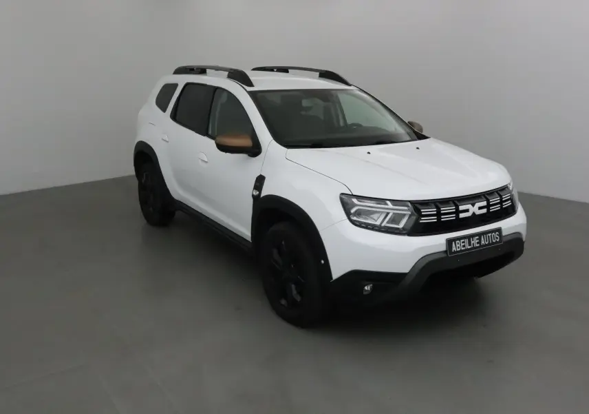 Dacia Duster 4x4 blanc en 3/4 avant droit avec rétroviseurs bronze et jantes noires dans un studio gris.