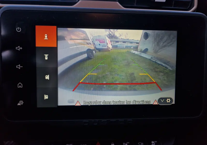 Vue de la caméra de recul du Dacia Duster blanc 2024, affichant les lignes d'aide au stationnement arrière.