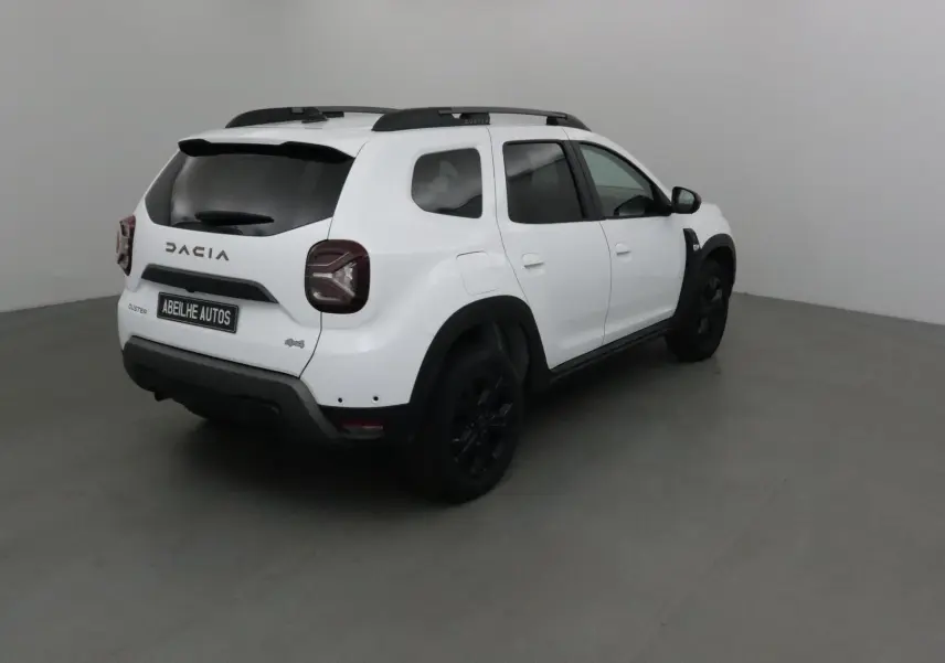 Vue 3/4 arrière droite d'un Dacia Duster blanc 4x4 2024 avec jantes noires et vitres teintées.