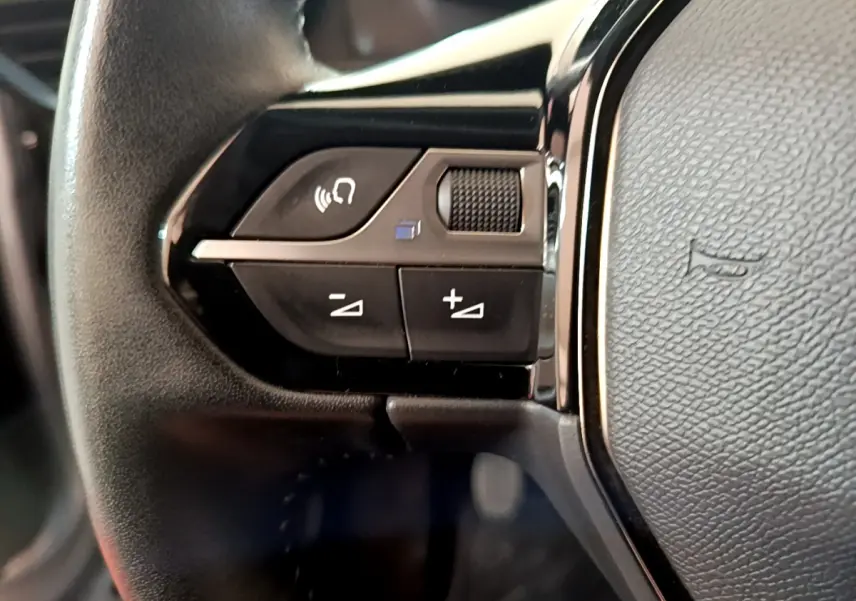 Gros plan sur les commandes gauche du volant cuir noir du Peugeot 2008 gris clair, version Allure Business 2021.