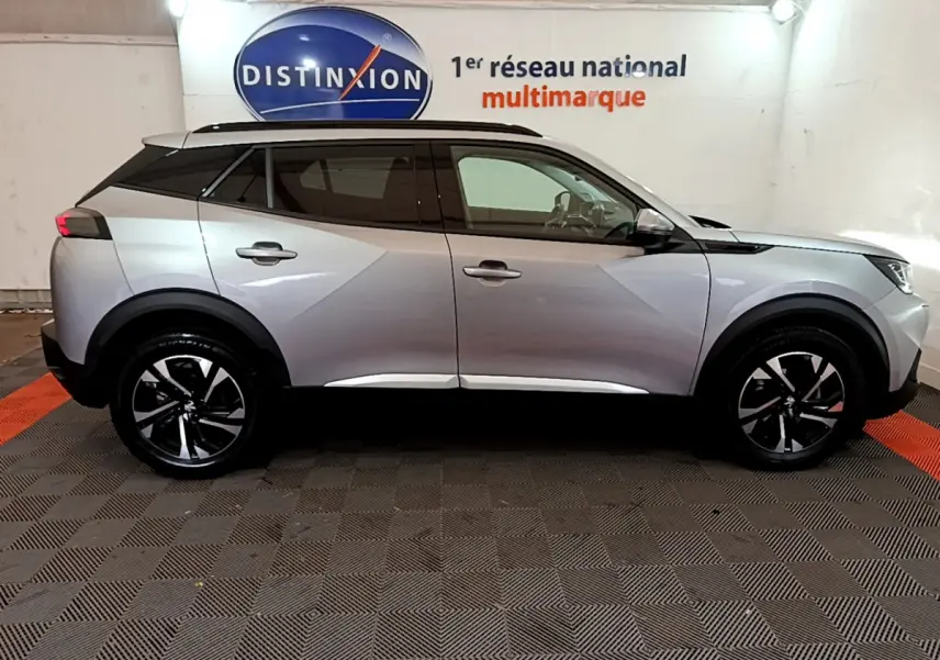Profil côté droit d'un Peugeot 2008 gris clair 2021 avec jantes noires et toit noir en showroom.