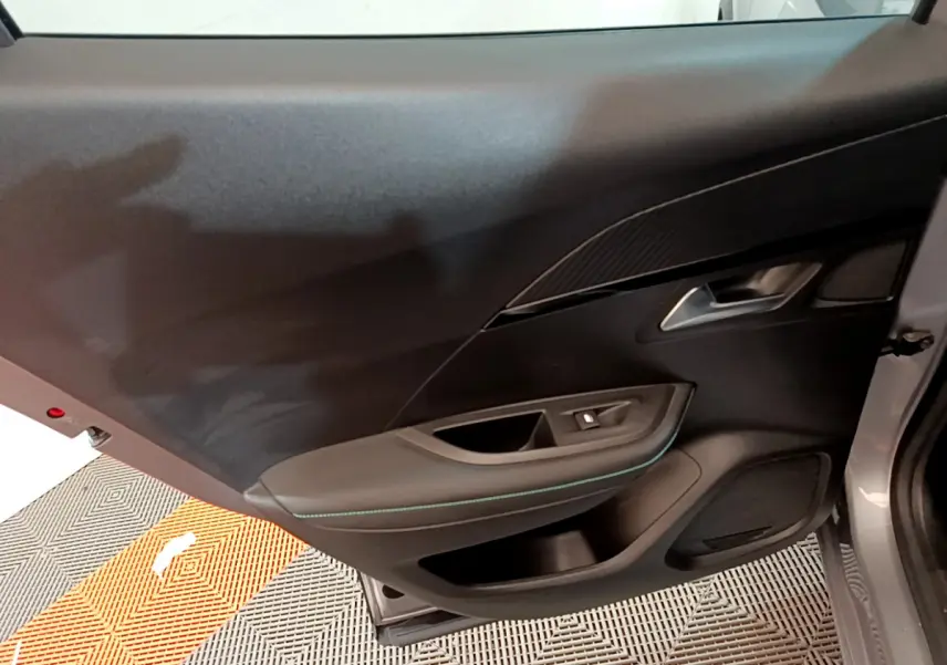 Vue intérieure de la porte côté gauche d'une Peugeot 2008 gris clair, avec garniture noire et surpiqûres bleues.