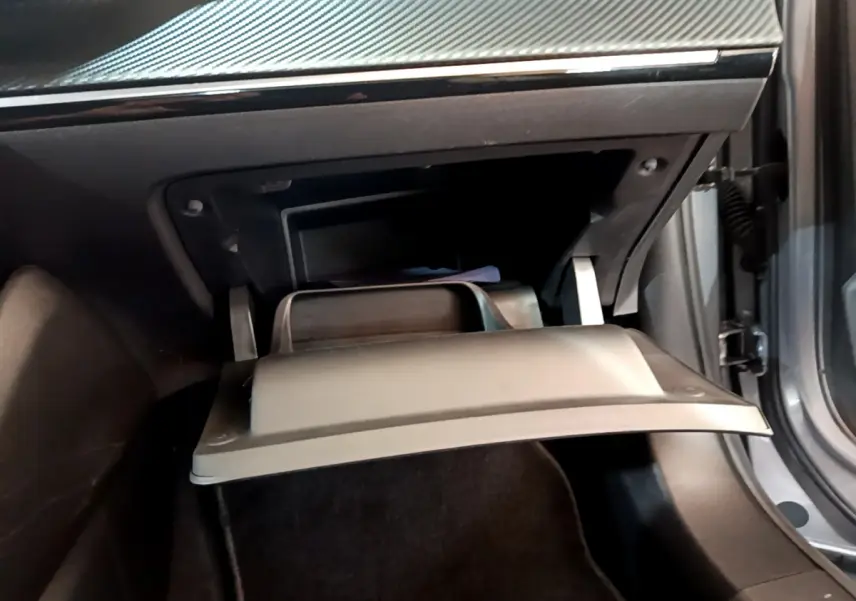 Gros plan sur la boîte à gants ouverte de la Peugeot 2008 gris clair, montrant l'intérieur noir et la portière côté droit entrouverte.