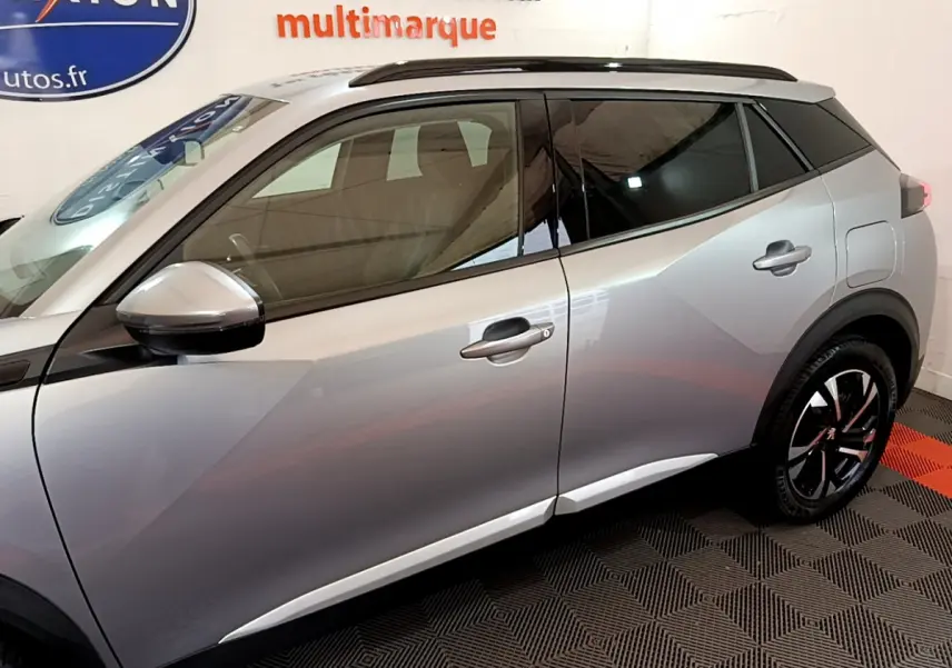Profil côté gauche d'un Peugeot 2008 gris clair 2021 avec jantes noires et toit noir en intérieur showroom.