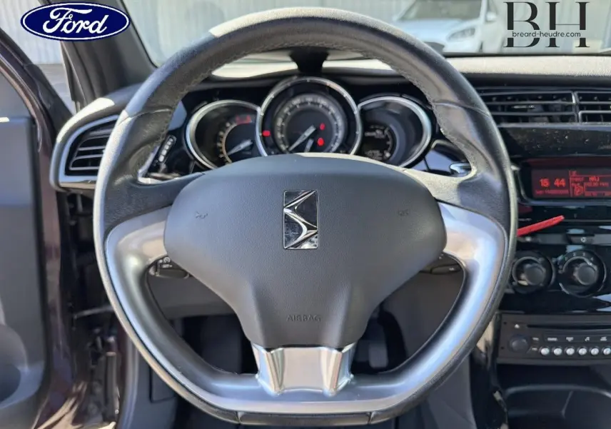 Vue intérieure centrée sur le volant DS3 avec logo Citroën, tableau de bord et console noire brillante.