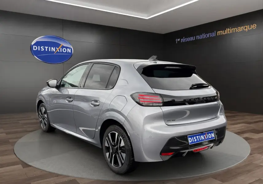 Peugeot 208 gris clair vue 3/4 arrière droit en intérieur, avec feux arrière LED et jantes alliage bicolores.