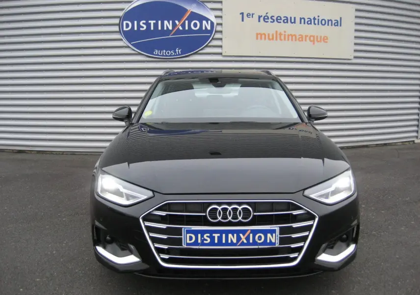 Vue frontale d'une Audi A4 Avant noire 2022 avec phares allumés et calandre chromée, devant un mur métallique.