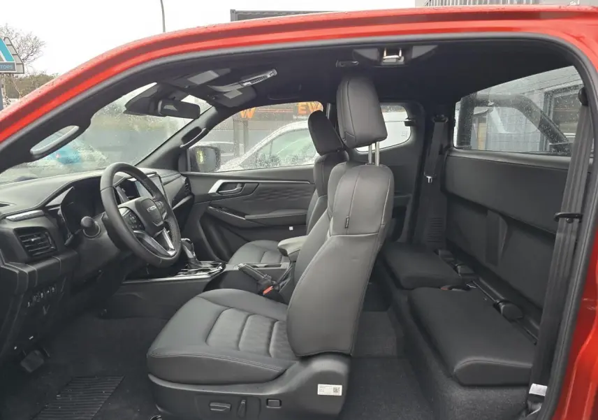 Vue intérieure côté gauche du pick-up Isuzu D-MAX orange métal, sièges en cuir noir et tableau de bord moderne.