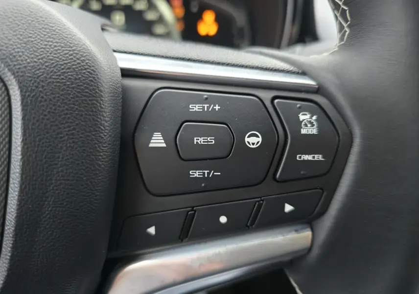 Gros plan sur les commandes au volant à droite de l'Isuzu D-MAX 2025, boutons noirs avec fonctions de régulateur et assistance.