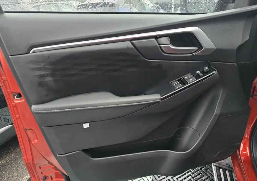 Vue intérieure de la porte côté gauche d'un Isuzu D-MAX orange métallisé avec commandes de vitres et poignée chromée.