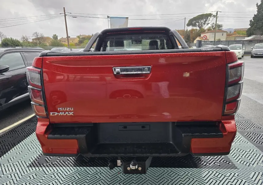 Vue arrière d'un pick-up Isuzu D-MAX orange métallisé avec attelage et hayon fermé sous la pluie.