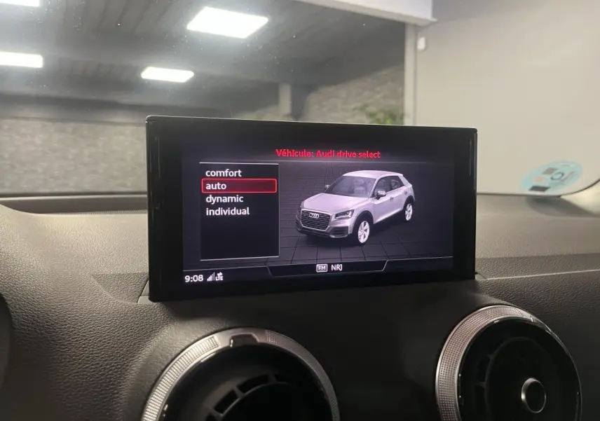 Écran central montrant un Audi Q2 gris en vue 3/4 avant avec options de mode de conduite sur fond noir.