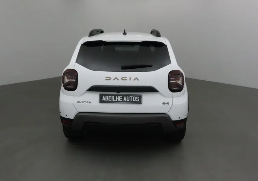 Vue arrière d'un Dacia Duster blanc 4x4 2024 avec logo et feux caractéristiques, en intérieur neutre.