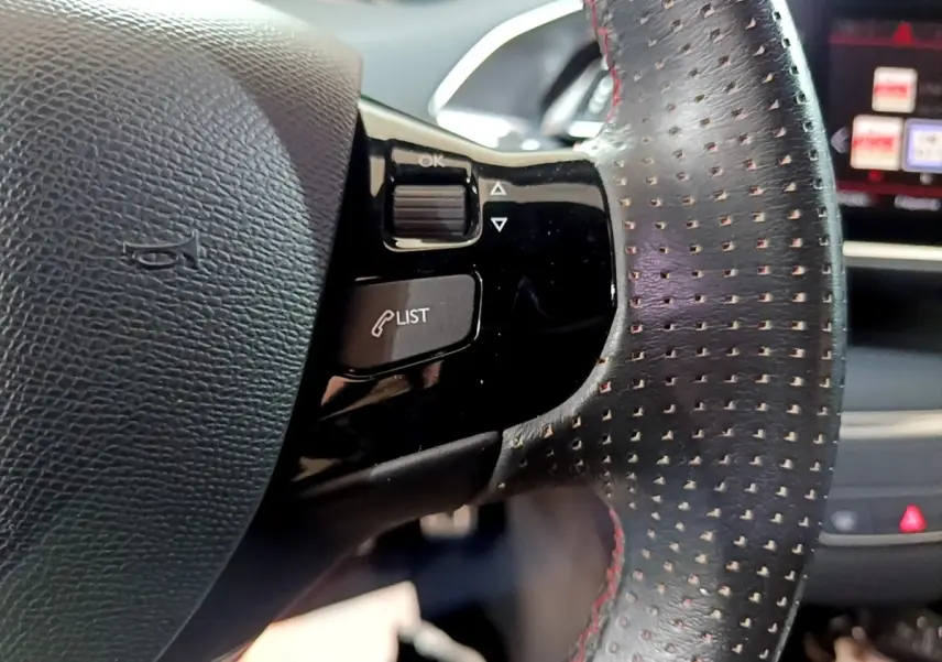 Gros plan sur le volant cuir perforé avec commandes intégrées du Peugeot 308 GT Line blanc, tableau de bord en arrière-plan.