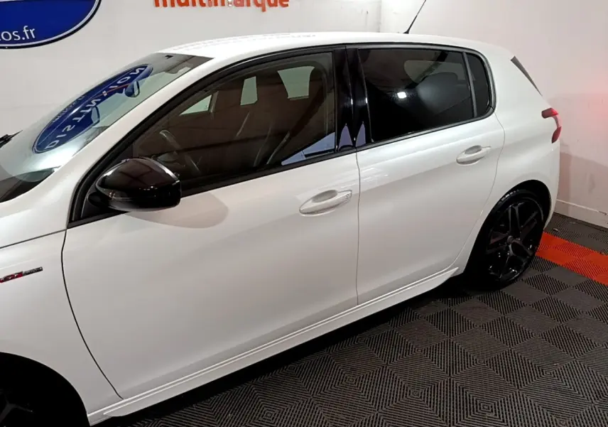 Profil côté gauche d'une Peugeot 308 GT Line blanche avec rétroviseurs noirs et jantes alliage foncé.
