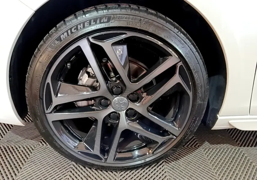 Gros plan sur la roue avant gauche noire brillante de la Peugeot 308 blanche Puretech 130 S&S GT Line 2019