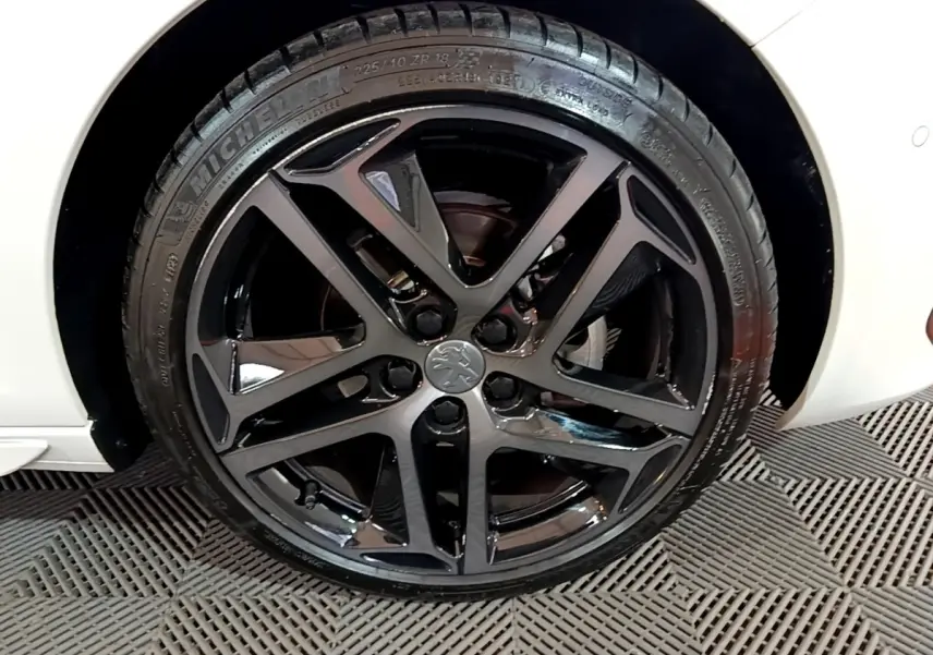 Gros plan sur la roue avant droite noire brillante d'une Peugeot 308 blanche Puretech 130 S&S GT Line 2019.