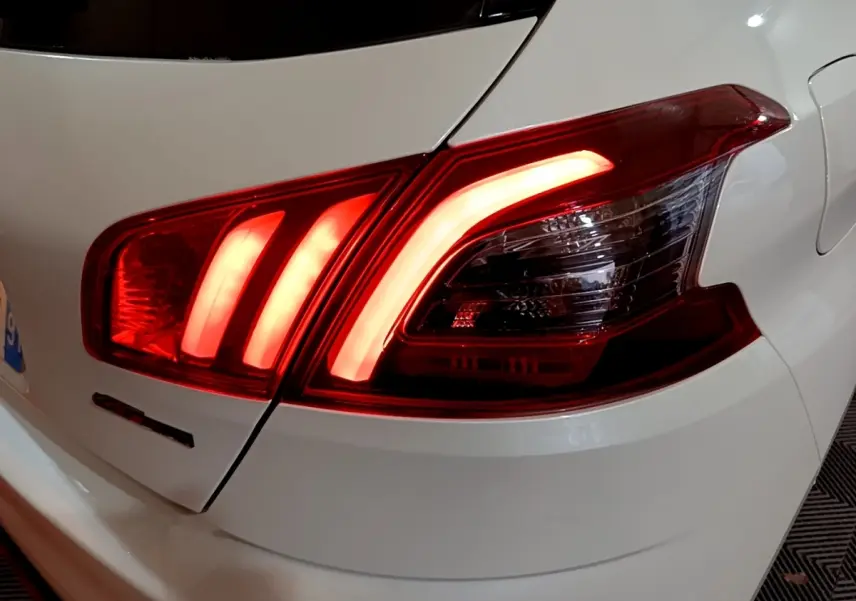 Gros plan sur le feu arrière droit allumé d'une Peugeot 308 blanche, version GT Line, soulignant ses lignes LED distinctives.