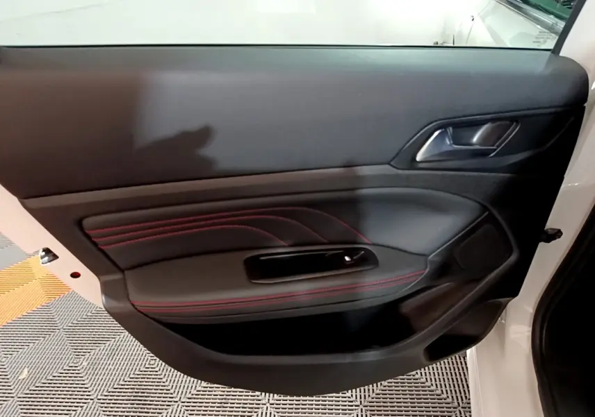 Gros plan sur la porte côté gauche d'une Peugeot 308 blanche, avec surpiqûres rouges et poignée intégrée.