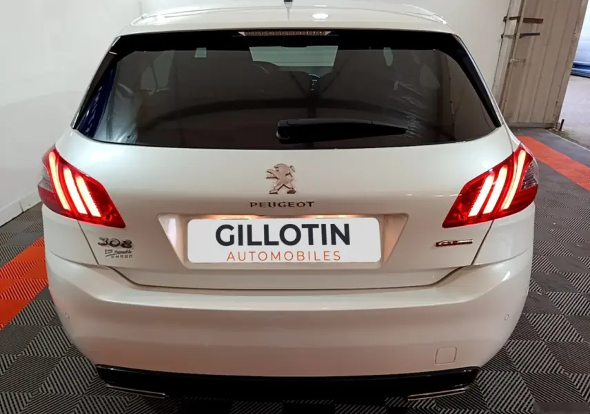 Vue arrière d'une Peugeot 308 blanche avec feux arrière allumés dans un garage fermé.