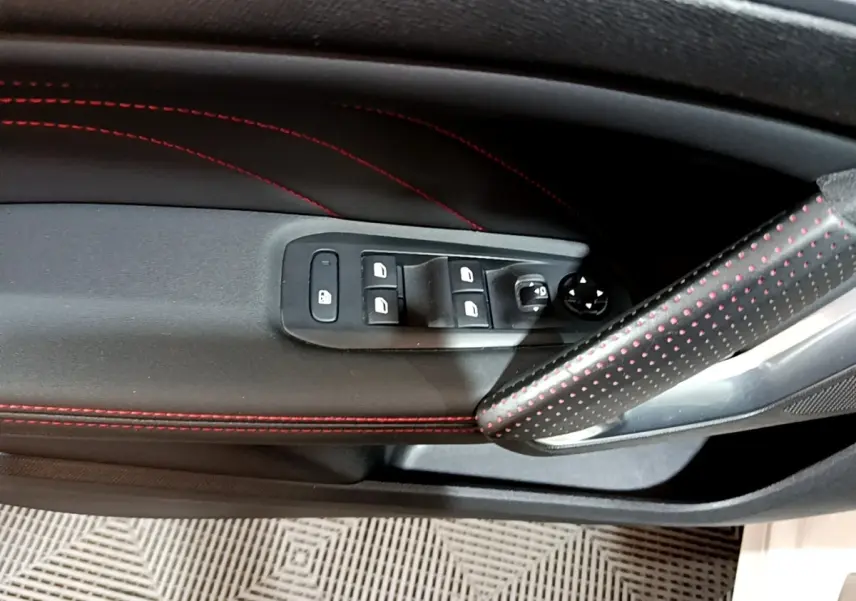 Gros plan sur la porte côté gauche de la Peugeot 308 GT Line blanche, avec surpiqûres rouges et commandes des vitres.