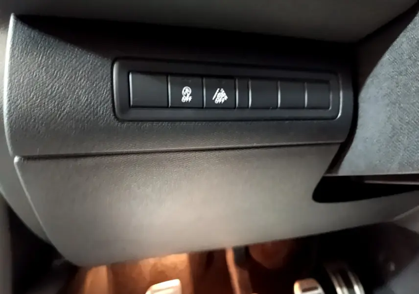 Gros plan sur les boutons de contrôle noirs sous le tableau de bord côté conducteur d'une Peugeot 308 blanche 2019.