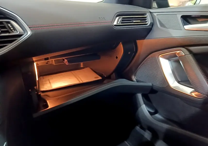 Intérieur de la Peugeot 308 GT Line 2019, vue côté passager sur boîte à gants ouverte avec éclairage intérieur.