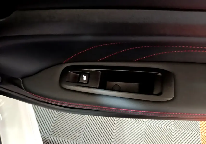 Détail de la poignée intérieure côté gauche avec surpiqûres rouges sur le panneau de porte noir d'une Peugeot 308 GT Line blanche.