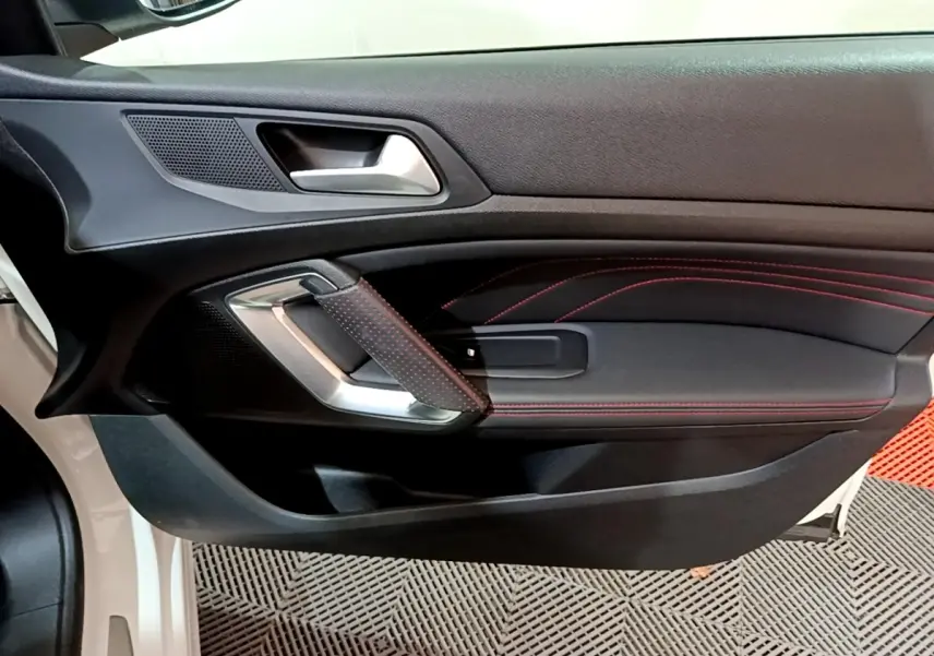 Gros plan sur la porte côté gauche d'une Peugeot 308 GT Line blanche, avec surpiqûres rouges et poignée argentée.