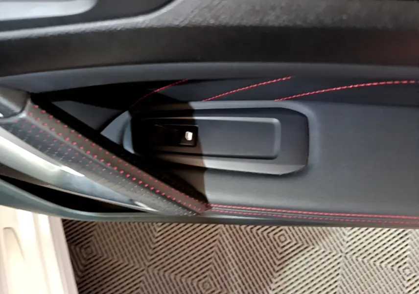 Détail de la poignée intérieure côté gauche avec surpiqûres rouges sur la porte noire de la Peugeot 308 GT Line blanche.