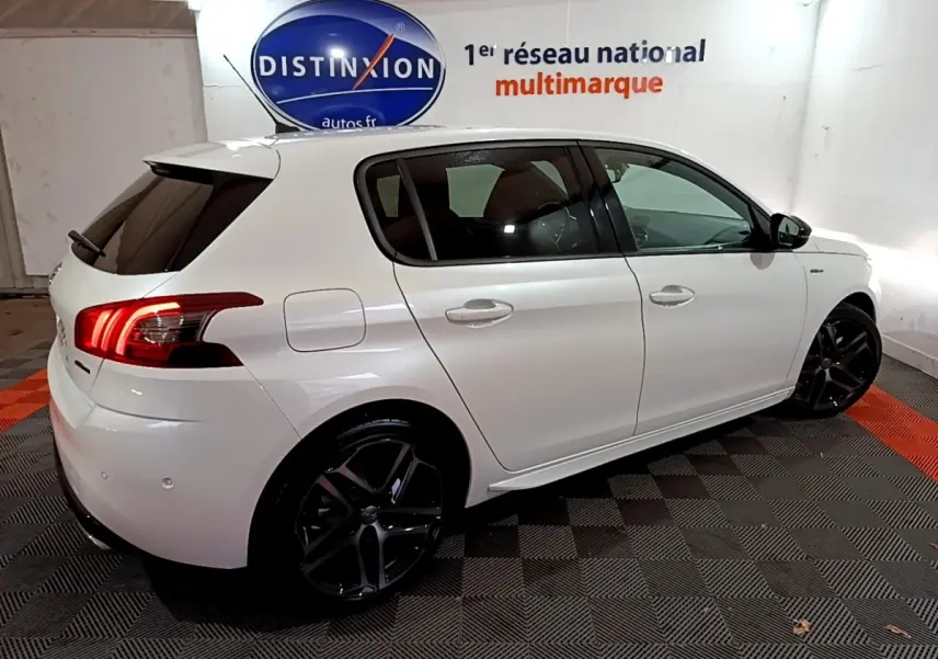 PEUGEOT 308 blanc vue côté droit arrière en intérieur, avec jantes noires et feux arrière allumés.