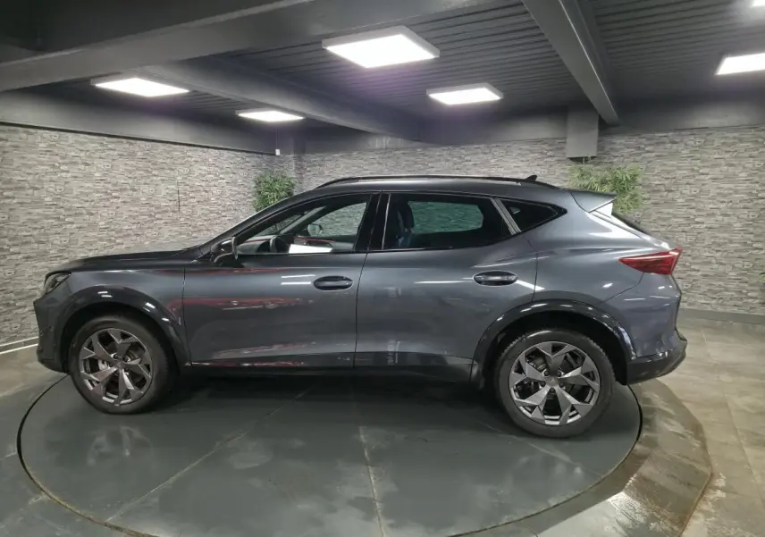 Vue de profil côté gauche d'un CUPRA Formentor gris métallisé 2025 avec jantes alliage 18'' et toit noir dans un garage.