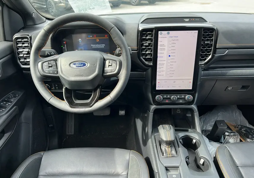 Vue intérieure avant du Ford Ranger 2026, tableau de bord noir avec écran tactile vertical et volant cuir multifonctions.