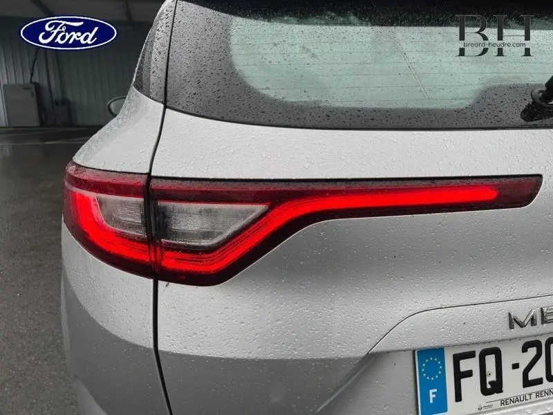 Gros plan sur le feu arrière droit rouge d'une Renault Mégane Break gris platine sous la pluie, avec partie de la plaque visible.